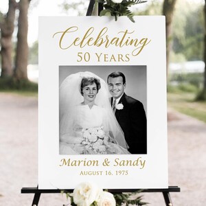 May include: White sign with gold text celebrating 50 years of marriage. The sign features a black and white photo of a couple on their wedding day and the text "Celebrating 50 Years", "Marion & Sandy", and "August 16, 1975".