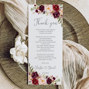 May include: A rectangular thank you card with floral accents in burgundy, pink, and green. The card features the words "Thank you" in elegant script, along with a message of gratitude. The card is set on a decorative plate with a fabric overlay.