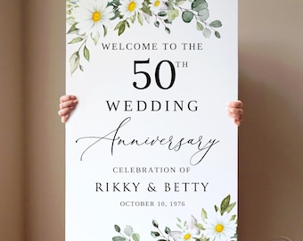 May include: A white sign with the text "WELCOME TO THE 50TH WEDDING ANNIVERSARY" and the names "RIKKY & BETTY" with the date "OCTOBER 10, 1976". The sign is decorated with watercolor daisies and greenery.
