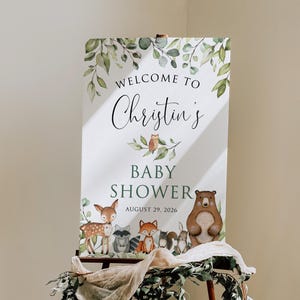 May include: A white sign with green foliage and woodland animals announcing "Welcome to Christin's Baby Shower August 29, 2026".