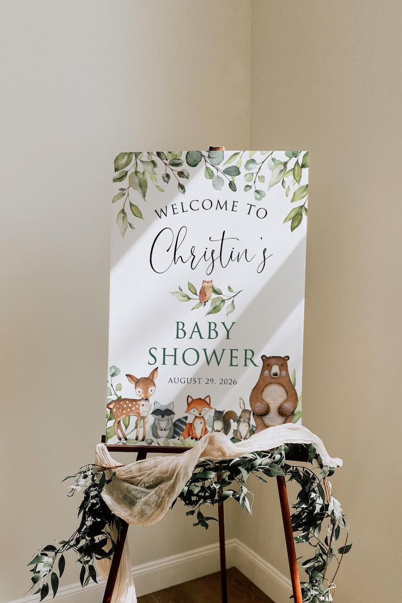 May include: A white sign with green foliage and woodland animals announcing "Welcome to Christin's Baby Shower August 29, 2026".