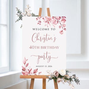 May include: A white welcome sign with pink floral accents. The sign reads "Welcome to Christin's 40th Birthday Party August 15, 2026".