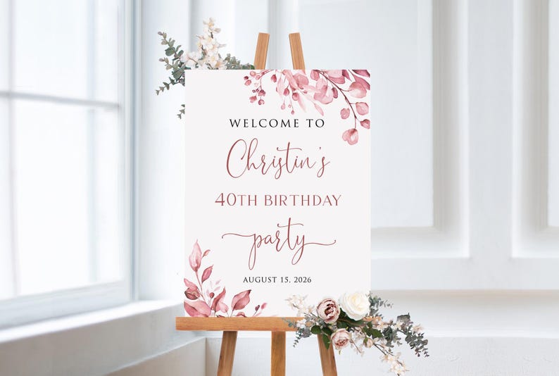 May include: A white welcome sign with pink floral accents. The sign reads "Welcome to Christin's 40th Birthday Party August 15, 2026".