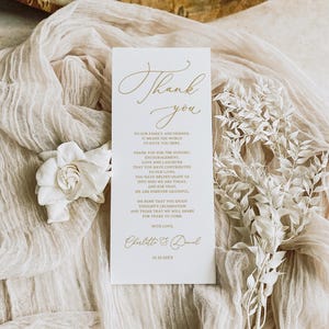 May include: A white card with gold lettering that says "Thank you" and expresses gratitude to family and friends for their support and love. The card is signed "Charlotte & Daniel" and includes the date "10.10.20XX".