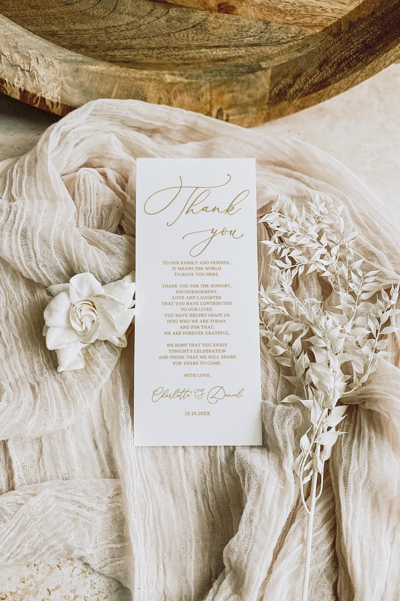 May include: A white card with gold lettering that says "Thank you" and expresses gratitude to family and friends for their support and love. The card is signed "Charlotte & Daniel" and includes the date "10.10.20XX".