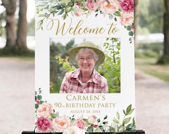 Puede incluir: Un letrero de bienvenida blanco con una foto de una mujer sonriente con sombrero y camisa a cuadros. El letrero está decorado con flores rosas y blancas y vegetación. El texto dice "Bienvenida a" y "90 cumpleaños de Carmen".