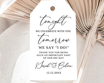 May include: A white tag with a rounded top and a hole at the top. The tag has black cursive text that reads "Tonight, We celebrate with you, Tomorrow, We say "I do!", Thank you for being such an important part of our big day, Sarah & Calvin, 12.12.20XX."