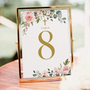 May include: A gold-framed table number card with the number 8 in gold. The card features floral watercolor accents with pink roses and greenery. The word "TABLE" and a cross are at the top.