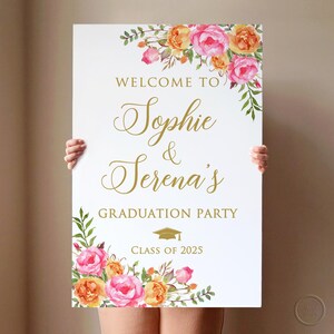May include: White welcome sign with gold lettering and floral accents. The sign reads "Welcome to Sophie & Serena's Graduation Party Class of 2025".