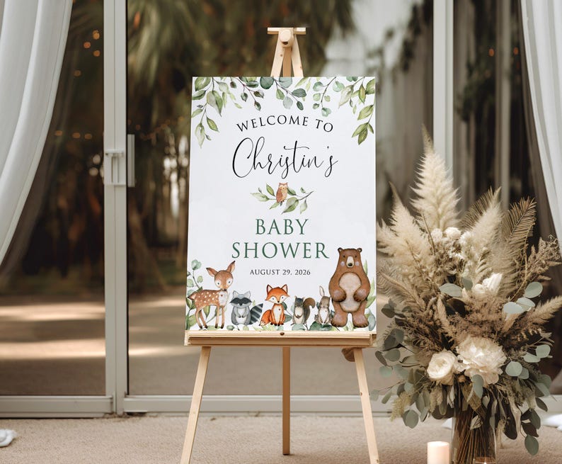 May include: Welcome to Christin's Baby Shower sign with a woodland theme. The sign features a brown bear, a fox, a deer, a raccoon, and a squirrel. The sign is on a wooden easel and has a green leafy border.