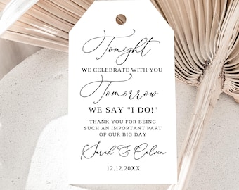 May include: A white tag with a rounded top and a hole, featuring elegant black script. The text reads "Tonight, We Celebrate With You, Tomorrow We Say 'I Do!'" and includes names and a date, perfect for wedding favors.