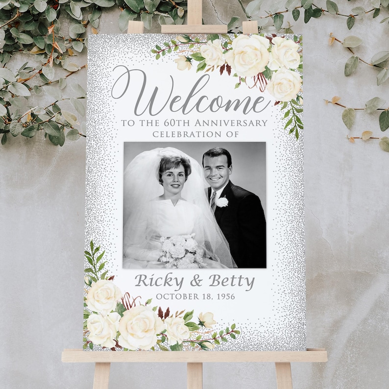 May include: A welcome sign for a 60th-anniversary celebration. The sign features a black and white photo of a couple, surrounded by floral accents and the words "Welcome" and "Ricky & Betty".