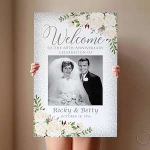 May include: A welcome sign for a 60th anniversary celebration. The sign features a black and white photo of a couple, surrounded by floral and glittery accents. The text reads "Welcome" and "Ricky & Betty October 18, 1956."