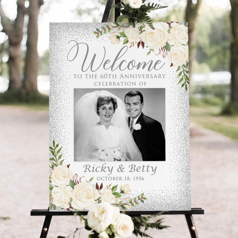 May include: A wedding welcome sign with a black and white photo of a couple. The sign has the words "Welcome" and "To the 60th Anniversary Celebration of" in gray script. The names "Ricky & Betty" and the date "October 18, 1956" are also displayed.
