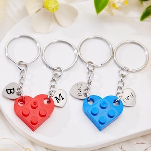 May include: Two keychains with heart-shaped charms. One keychain has a red heart-shaped charm with the letter "B" on a silver heart charm. The other keychain has a blue heart-shaped charm with the letter "M" on a silver heart charm. Both keychains have a silver ring.
