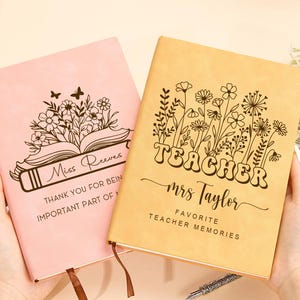 May include: Two personalized notebooks, one pink and one tan, are displayed. The pink notebook features a floral design and the text "Miss Reeves." The tan notebook has the word "TEACHER" and the name "Mrs. Taylor." Both notebooks are for teachers.