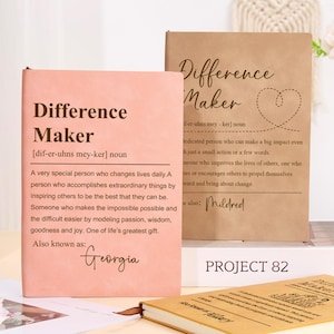 May include: Notebooks with the words "Difference Maker" printed on the covers. One is pink with "Georgia" printed on it, the other is tan with "Mildred". The notebooks are for journaling or note-taking.