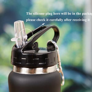 May include: Close-up of a black water bottle with a black lid and a clear straw. The lid has a handle and a silver ring for attaching a carabiner. Text on the image reads: "The silicone plug here will be in the packaging box, please check it carefully after receiving it."