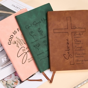 May include: Three leather-bound journals with inspirational quotes and floral designs. The pink journal says "God is faithful in every season". The green journal says "God says you are beautiful, enough, amazing, loved". The brown journal says "Sabrina" and has a cross with the words "You are beautiful, strong, enough, never alone, always loved".