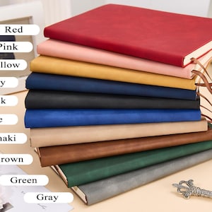 May include: A stack of ten notebooks in various colors, including red, pink, yellow, navy, black, blue, khaki, brown, green, and gray. The notebooks are made of leather and have a simple design.