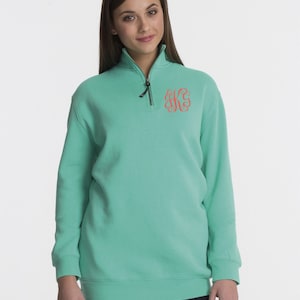 May include: A turquoise green quarter-zip sweatshirt with a monogrammed initial on the chest. The monogram is in a coral pink color.