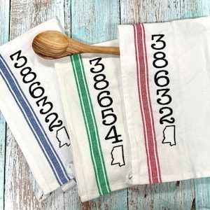 May include: Three white kitchen towels with blue, green, and red stripes. Each towel has a black outline of the state of Mississippi and the numbers 386322.