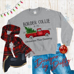 May include: A gray sweatshirt with a red truck carrying a Christmas tree. The truck has a dog in the driver's seat and the text "BORDER COLLIE & CO EST 1995 Christmas Tree Delivery".