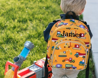 May include: A yellow construction vehicle backpack with a black strap and a name tag that says "James". The backpack is decorated with a variety of construction vehicles, including trucks, excavators, and bulldozers.