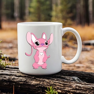 May include: White ceramic mug featuring a pink cartoon character with large ears and a purple nose. The character is standing with its hands clasped. The mug has a curved handle and is set against a blurred outdoor background.
