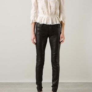 May include: A cream blouse with lace inserts and a high neck, worn with black, textured trousers. The trousers have a snakeskin effect. The outfit is finished with strappy heels.