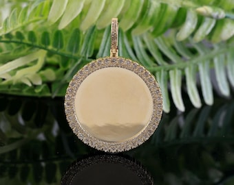 May include: A gold pendant with a round, blank surface surrounded by a border of small, clear stones.