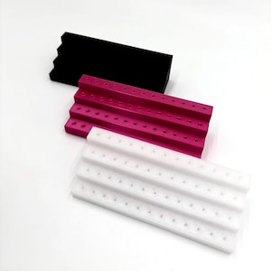 Può includere: Tre espositori per orecchini a più livelli in nero, magenta e bianco. Ogni espositore ha più file di piccoli fori per contenere gli orecchini. Gli espositori sono realizzati in un materiale solido e sono progettati per esporre gioielli.