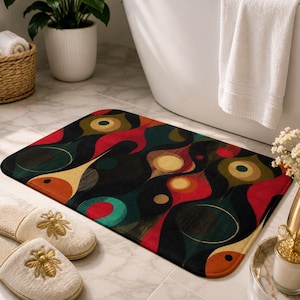 May include: A rectangular bath mat with an abstract design in black, red, teal, and gold. The pattern features organic shapes and curves. The mat is placed on a tiled floor near a bathtub and a pair of slippers.