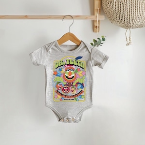 May include: A gray baby onesie with a colorful graphic of Dr. Teeth and the Electric Mayhem from The Muppets. The graphic includes the text "Dr. Teeth & The Electric Mayhem World Tour".