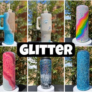 May include: A selection of glitter tumblers in diverse colours and designs. Some tumblers have text, others feature rainbow, beach, and abstract patterns. The tumblers are displayed on white stands against a natural background.