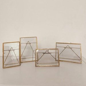 May include: Four gold-toned metal picture frames with glass panels. The frames are arranged in a row, with the largest frame at the back and the smallest frame at the front. The frames are all empty.