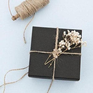 May include: A black gift box wrapped with twine and decorated with a sprig of white dried flowers.