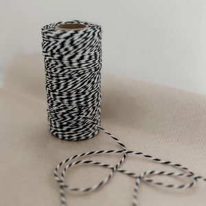 May include: A roll of black and white baker's twine with a length of twine extending from the roll.