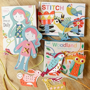 May include: A selection of children's craft kits from the "Learn to Stitch" range. The kits feature illustrated cardboard cutouts of a doll, birds, and woodland creatures, with pre-punched holes for stitching with yarn. The boxes are white with colourful illustrations.