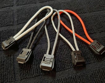 Puede incluir: Cinco tiradores de cremallera de diferentes colores, incluyendo negro, blanco, gris y naranja. Los tiradores de cremallera están hechos de cordón y tienen un deslizador de plástico.