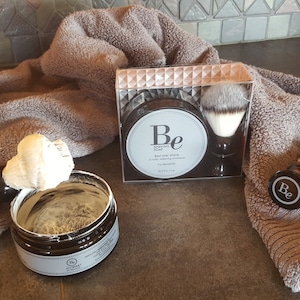 Puede incluir: Un primer plano de un juego de jabón de afeitar con una etiqueta en blanco y negro que dice "Be Shaving Soap". El juego incluye un jabón de afeitar, una brocha de afeitar y una segunda brocha de afeitar con un mango negro y una etiqueta blanca que dice "Be".
