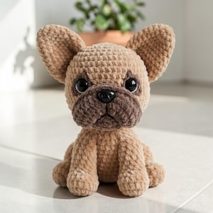 May include: A handmade, plush, light brown French Bulldog dog. The dog has large, floppy ears, a dark brown muzzle, and black eyes. The dog is sitting upright on a light-colored surface.