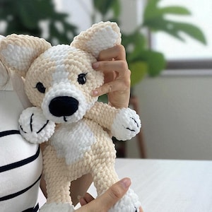 Op de afbeelding: Een handgemaakt pluchen hondenspeelgoed in crème en wit. De hond heeft een zwarte neus, zwarte ogen en witte poten. Het speelgoed wordt vastgehouden door een persoon die een gestreept shirt draagt. De hond is ongeveer 25 cm hoog.