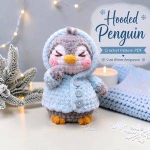 Op de afbeelding: Een gehaakte pinguïn amigurumi met een lichtblauw vest met capuchon en drie knopen, voorzien van een grijs lichaam, gele snavel en roze wangen. De tekst luidt Hooded Penguin Crochet Pattern PDF Cute Winter Amigurumi.