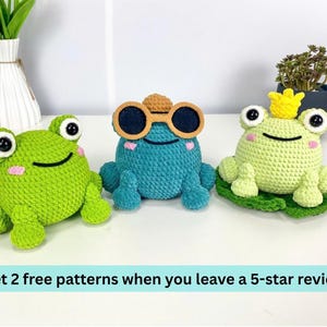 May include: Three crocheted frog plushies in green and teal. One frog wears sunglasses, another a crown, and the third is plain. The frogs have large eyes and smiling faces. Text at the bottom reads: Get 2 free patterns when you leave a 5-star review.