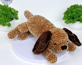 May include: A brown crocheted dog toy with brown felt ears. The dog is lying on its side with its eyes closed.