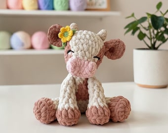 May include: A handmade crochet cow plushie in shades of brown, white, and pink. The cow has a flower on its head and is sitting down. The plushie is made of soft yarn and has a cute, friendly expression. The cow is a decorative item.