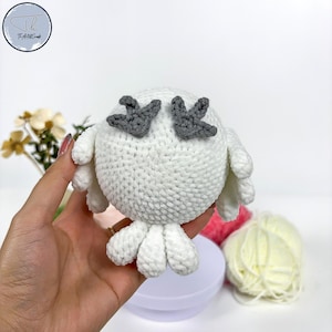 May include: White crocheted owl with gray felt wings. The owl is sitting on a hand.