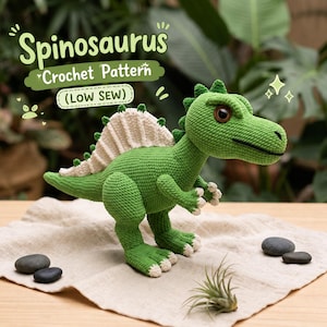 May include: A green crochet Spinosaurus dinosaur toy with a cream-colored dorsal fin, dark brown eyes, and white claws. The text above the toy reads Spinosaurus Crochet Pattern (Low Sew). The dinosaur is standing on a light-colored fabric cloth.