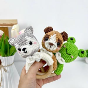May include: Crocheted baby rattles in the shape of a gray and white wolf, a brown and white dog, and a green frog. Each animal is attached to a wooden ring. The rattles are handmade and feature detailed facial features and soft textures.